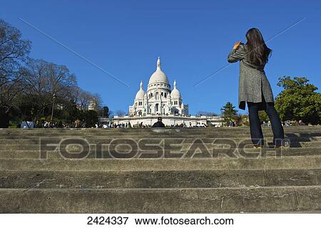 Stock Photo - Tourist stands on the steps and takes a photograph of the Basilica of the Sacred Heart of Paris; Paris, France. Fotosearch