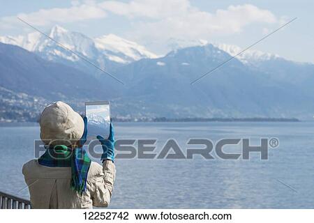 Tourist takes a photograph of the Swiss Alps and Lake Maggiore on her tablet; Brissago, Ticino, Switzerland View Large Photo Image Stock Image - Tourist takes a photograph of the Swiss Alps and Lake Maggiore on her tablet; Brissago, Ticino, Switzerland. Fotosearch