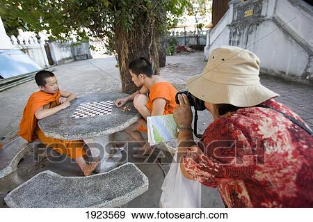 Stock Photo - Tourist Taking Photographs Of Young Novice Monks Playing Checkers, Luang Prabang, Laos. Fotosearch
