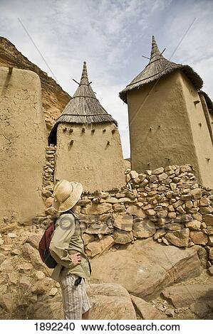 Stock Image - Tourist Walking Among Dogon Village Buildings. Fotosearch