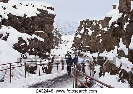 Tourists explore the rugged terrain on a snowy path; Thingvellir, Iceland View Large Photo Image Stock Photo - Tourists explore the rugged terrain on a snowy path; Thingvellir, Iceland. Fotosearch