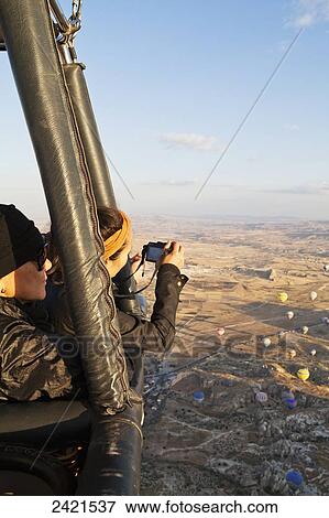 Stock Photo - Tourists in a hot air balloon taking pictures of the view below; Cappadocia, Turkey. Fotosearch