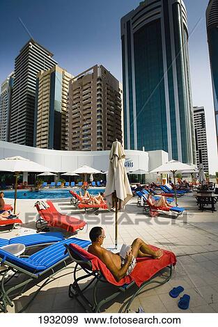 Stock Photo - Tourists Lounging On Deckchairs By Hotel Pool With Skyscrapers In Background, Dubai's International Financial Centre, Sheikh Zayed Road Dubai, Uae. Middle East. Fotosearch