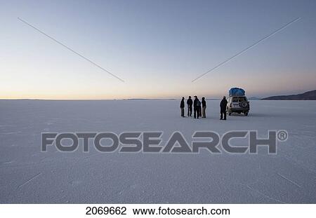 Stock Image - Tourists Next To A 4X4 Vehicle On The Salar De Uyuni, The World's Largest Salt Flat At Dawn, Potosi Department, Bolivia. Fotosearch