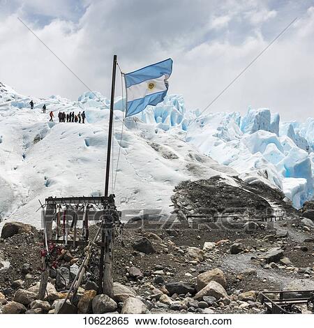 Stock Photography - Tourists on Moreno glacier with the Argentinian flag in the foreground, Los Glaciares National Park; Santa Cruz province, Argentina. Fotosearch