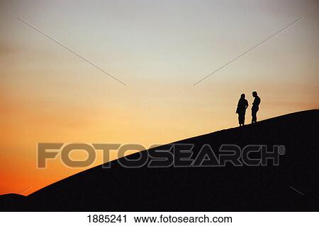 Stock Image - Tourists On Sand Dune At Sunset, Ubari Sand Sea. Fotosearch