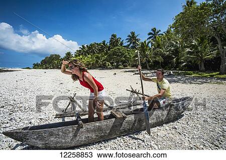 Stock Image - Tourists playing in a wooden boat on the beach; Tanna Island, Vanuatu. Fotosearch