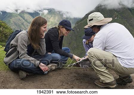 Stock Image - Tourists Read From A Guide At The Lost City Of Inca; Machu Picchu Peru. Fotosearch