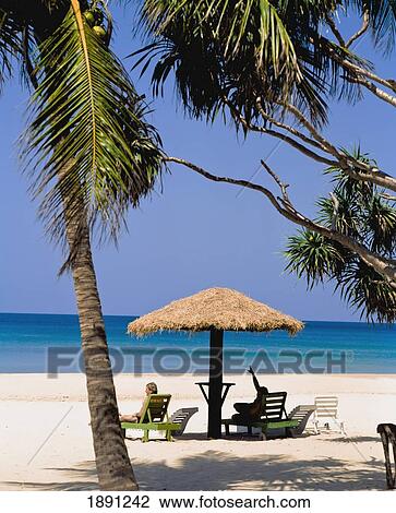Tourists Relaxing On Sun Loungers Under Thatched Umbrella On Beach View Large Photo Image Stock Image - Tourists Relaxing On Sun Loungers Under Thatched Umbrella On Beach. Fotosearch