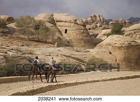 Stock Image - Tourists Ride On Horses To Explore; Petra Jordan. Fotosearch