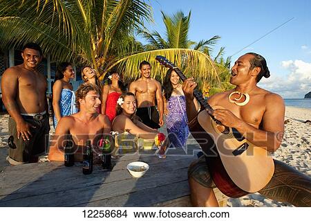 Picture - Tourists singing along with a Samoan guitar player on the beach; Upulu Island, Samoa. Fotosearch