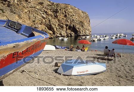 Stock Photography - Tourists Sitting On Beach Under Umbrellas Near Fishing Boats. Fotosearch