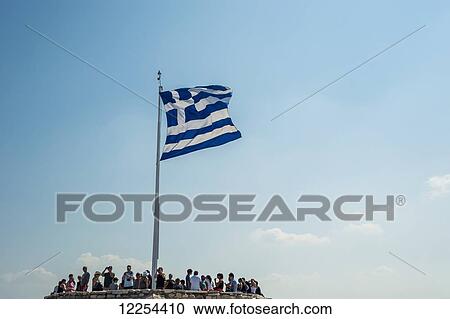 Stock Image - Tourists stand at a lookout point at the Acropolis with the flag of Greece flying overhead; Athens, Greece. Fotosearch