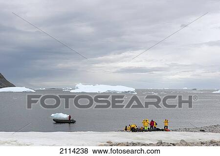 Stock Photo - Tourists Stand At The Coastline With A View Of An Iceberg; Antarctica. Fotosearch