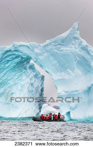 Stock Image - Tourists view floating iceberg, Cierva Cove, Western Antarctic Peninsula; Antarctica. Fotosearch