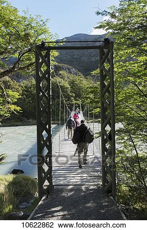 Stock Image - Tourists walking on a bridge over a river, Torres del Paine National Park; Torres del Paine, Magallanes and Antartica Chilena Region, Chile. Fotosearch