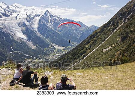 Stock Photo - Tourists watching paraglider flight at take-off point above Chamonix-Mont Blanc valley, with Mont Blanc mountain in background; France. Fotosearch