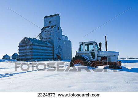 Stock Image - Tractor with old grain elevator in the background; Benson, Saskatchewan, Canada. Fotosearch