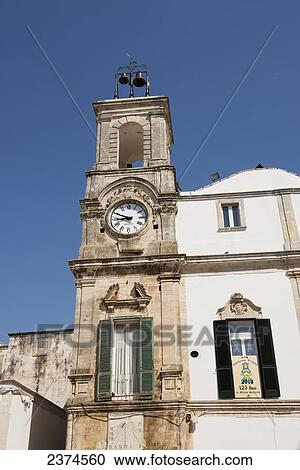 Stock Image - Traditional Puglian architecture with old clock and green wooden window shutters; Martina Franca, Puglia, Italy. Fotosearch