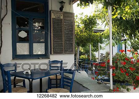 Stock Image - Traditional wooden chairs and red geraniums outside a taverna; Apollonia, Sifnos, Cyclades, Greek Islands, Greece. Fotosearch