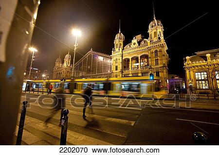 Stock Image - Tram And People Crossing In Front Of Budapest Western Railway Station At Night, Budapest, Hungary. Fotosearch