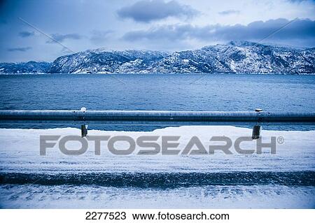 Stock Image - Treacherous icy road winding around the mountainside and Fjord shoreline with dramatic view of the mountains; Ortnevik, Sognefjord, Norway. Fotosearch