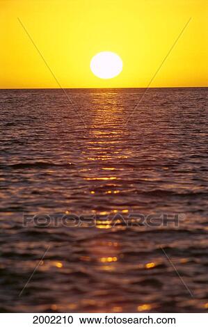 Stock Image - Tropical Sunset With Yellow Sky, Sun Ball Over Ocean, Shimmering Reflections. Fotosearch