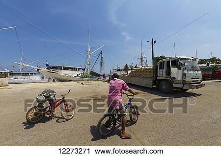 Stock Image - Truck laden with sacks by a Pinisi, a traditional two masted wooden cargo sailing ship moored in Paotere Harbour, Makassar (Ujung Pandang), South Sulawesi, Indonesia. Fotosearch