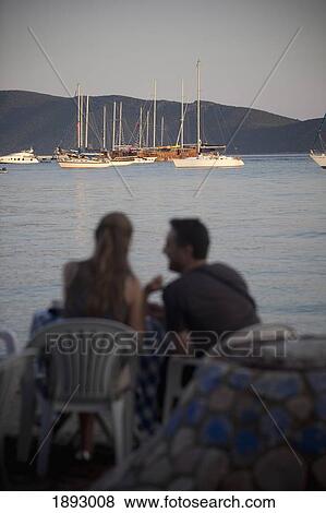 Stock Photo - Turkey, Couple sharing moment and drink on East Bay Beach of Bodrum With Views of Gulet Boats; Bodrum. Fotosearch