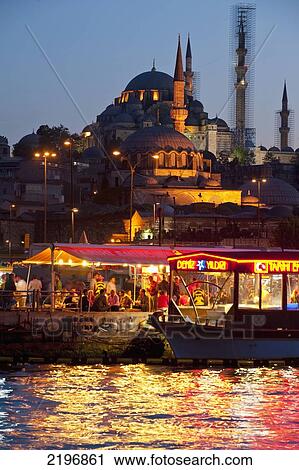 Stock Image - Turkey, Fish restaurants being run from side of boats beside Golden Horn with Suleymaniye mosque behind at dusk; Istanbul. Fotosearch