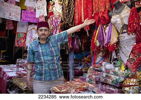 Stock Photography - Turkey, Stall Holder Pointing To His Belly Dancing Costumes And Traditional Dress Sold To Tourists On Display At Kapali Carsi (Grand Bazaar) Beyazit; Istanbul. Fotosearch