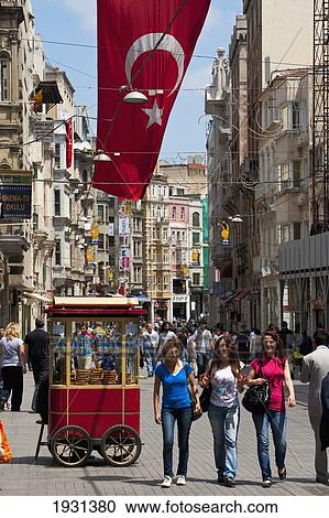 Stock Image - Turkey, Traditional Bread Seller and Crowds of People Walking Along Istiklal Caddesi Beneath Large Turkish Flag; Istanbul. Fotosearch