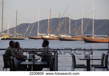 Stock Photo - Turkey, With Views Of Gulet Boats Moored Off Bay; Bodrum, Beachside Dining On East Bay Beach Of Bodrum. Fotosearch