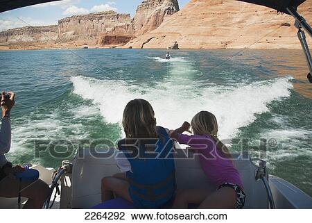 Stock Image - Two blond girls on back of speedboat watch their father on wakeboard behind speedboat on lake powell; page arizona usa. Fotosearch