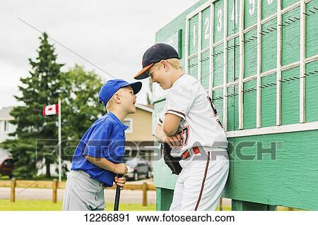 Two boys in baseball uniforms playfully argue in front of the scoreboard during a baseball game at a sports field; Fort McMurray, Alberta, Canada View Large Photo Image Stock Image - Two boys in baseball uniforms playfully argue in front of the scoreboard during a baseball game at a sports field; Fort McMurray, Alberta, Canada. Fotosearch