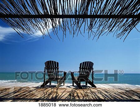 Stock Photo - Two Chairs On Deck By Ocean Shaded By Grass Roof. Fotosearch