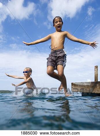 Stock Image - Two Children Jumping Off Pier Into The Ocean. Fotosearch