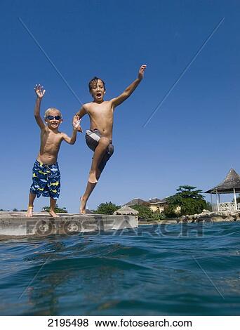 Stock Photo - Two Children Jumping Off Platform Into The Sea, Discovery Bay, Jamaica.. Fotosearch