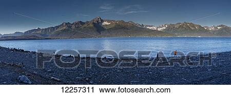 Stock Image - Two children throw rocks into Resurrection Bay at Seward Alaska, Southcentral, Summer. USA. Panorama.. Fotosearch