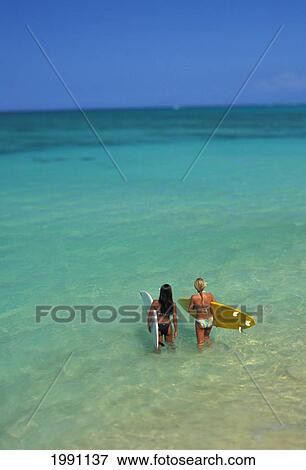 Stock Photo - Two Females Walk Into Ocean Holding Surfboards, View From Behind, Beautiful Turquoise Ocean Out To Horizon, Blue Sky. Fotosearch
