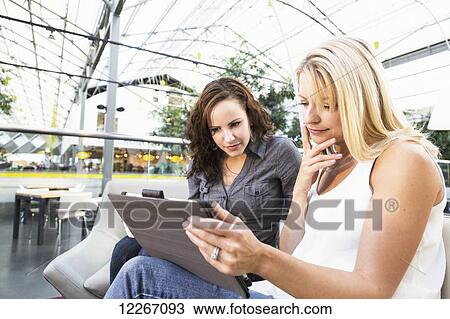 Two friends looking at a tablet while having coffee in a mall; St. Albert, Alberta, Canada View Large Photo Image Stock Image - Two friends looking at a tablet while having coffee in a mall; St. Albert, Alberta, Canada. Fotosearch