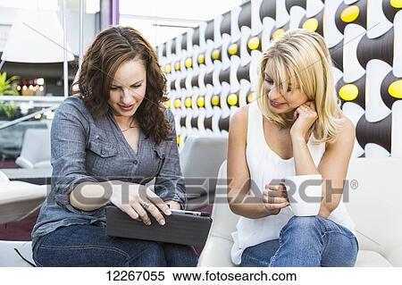 Stock Photography - Two friends looking at a tablet while having coffee in a mall; St. Albert, Alberta, Canada. Fotosearch
