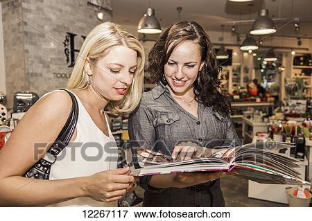 Two friends looking through cookbooks at a kitchen store in shopping mall; St. Albert, Alberta, Canada View Large Photo Image Stock Photo - Two friends looking through cookbooks at a kitchen store in shopping mall; St. Albert, Alberta, Canada. Fotosearch