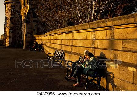Stock Photograph - Two friends talking on a bench at sunset; Edinburgh, Scotland. Fotosearch