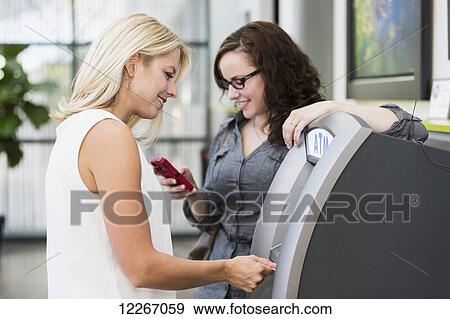 Stock Photo - Two girlfriends getting money from an ATM machine at the mall; St. Albert, Alberta, Canada. Fotosearch
