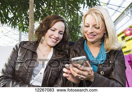 Two girlfriends out shopping together and taking a rest and checking messages; St. Albert, Alberta, Canada View Large Photo Image Stock Image - Two girlfriends out shopping together and taking a rest and checking messages; St. Albert, Alberta, Canada. Fotosearch