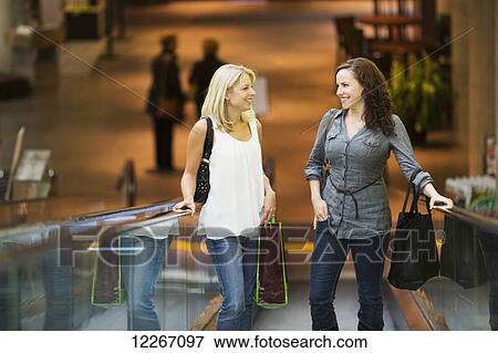 Stock Photo - Two girlfriends taking escalator while out shopping together; St. Albert, Alberta, Canada. Fotosearch