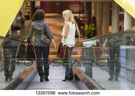 Stock Photograph - Two girlfriends taking escalator while out shopping together; St. Albert, Alberta, Canada. Fotosearch