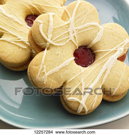 Picture - Two jam filled flower shaped sugar cookies on a teal plate; Victoria, British Columbia, Canada. Fotosearch
