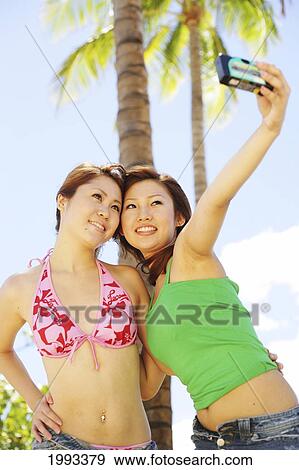 Stock Photo - Two Japanese Girls Take A Picture Of Themselves With Palm Trees Behind. Fotosearch
